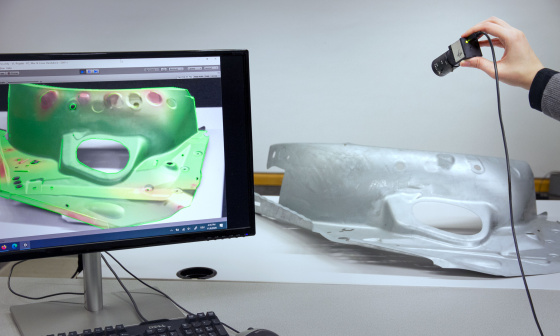 Eine Hand hält eine Industriekamera auf ein 3D-Modell, was daraufhin auf einem Bildschirm angezeigt wird.