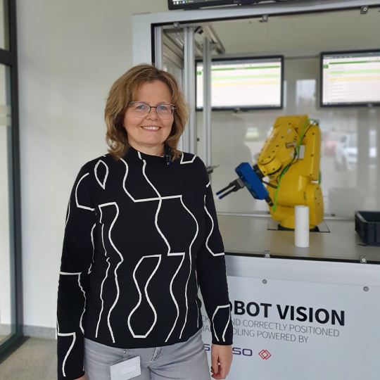 Sigrid Rögner steht vor dem Pick and Place Roboter Ervin der IDS.